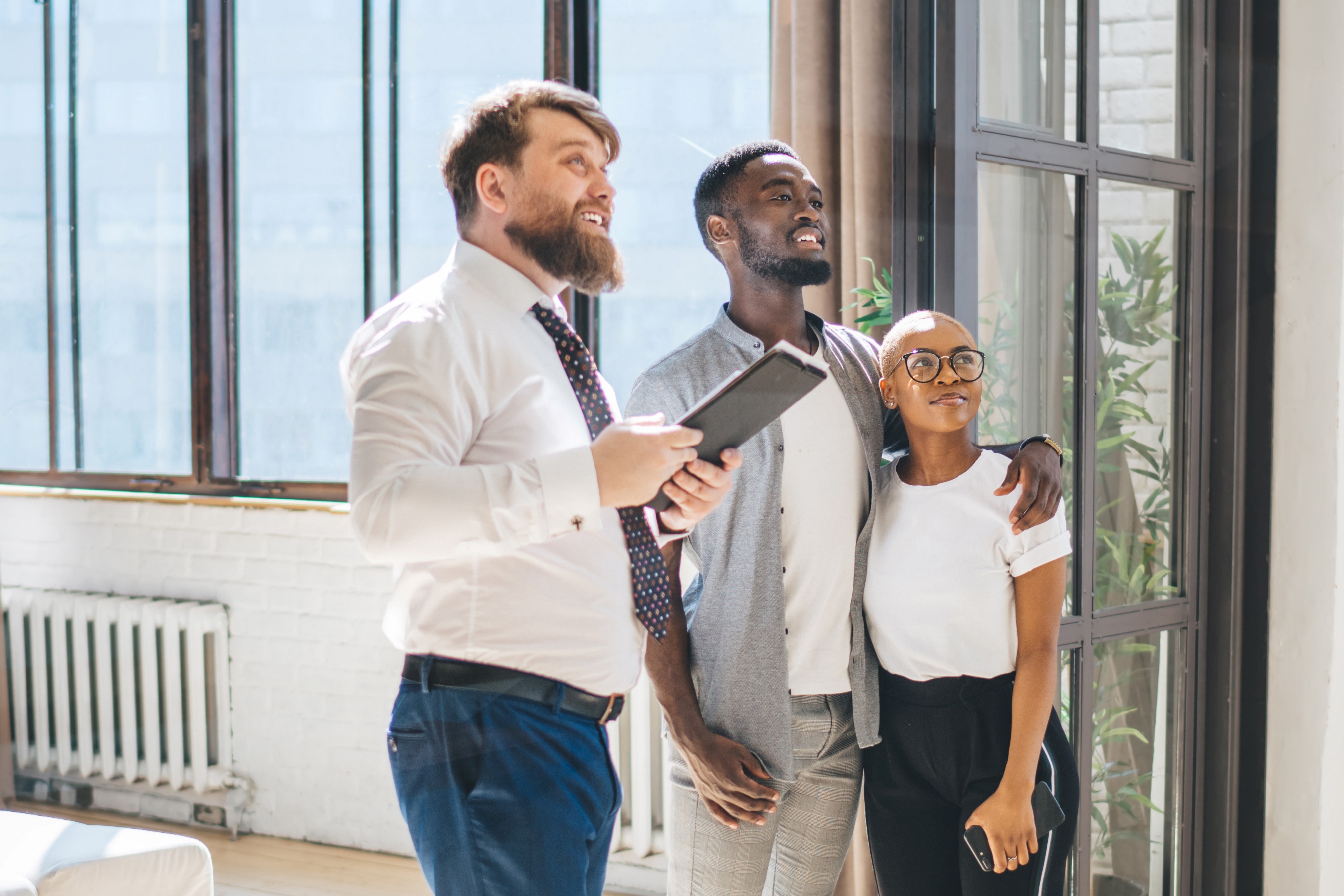Professional estate agent showing apartment to African American positive hugging couple